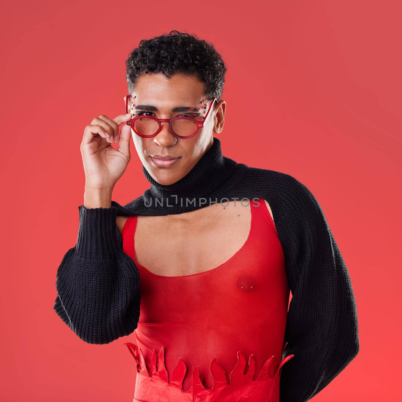 Fashion, portrait and gay man with glasses isolated on a red background in a studio. Lgbt, vision and stylish model person with fashionable eyewear, edgy clothes and funky style on a backdrop.