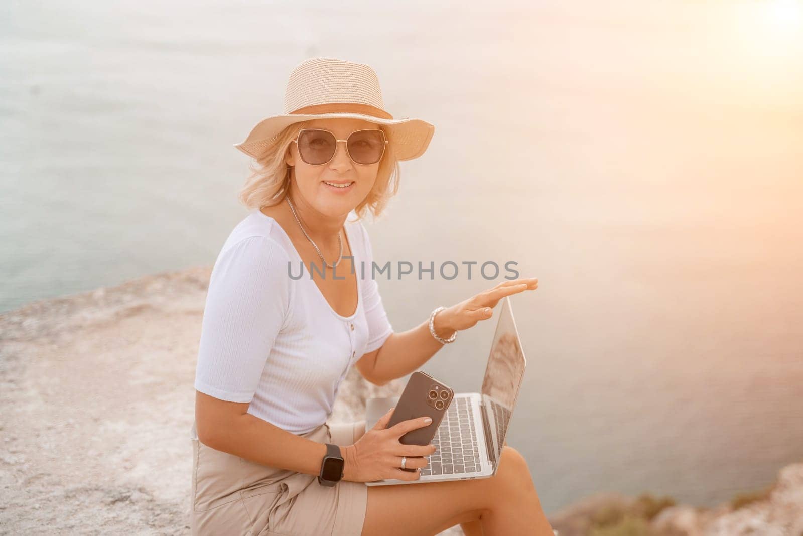 Freelance women sea working on the computer. Good looking middle aged woman typing on a laptop keyboard outdoors with a beautiful sea view. The concept of remote work. by Matiunina