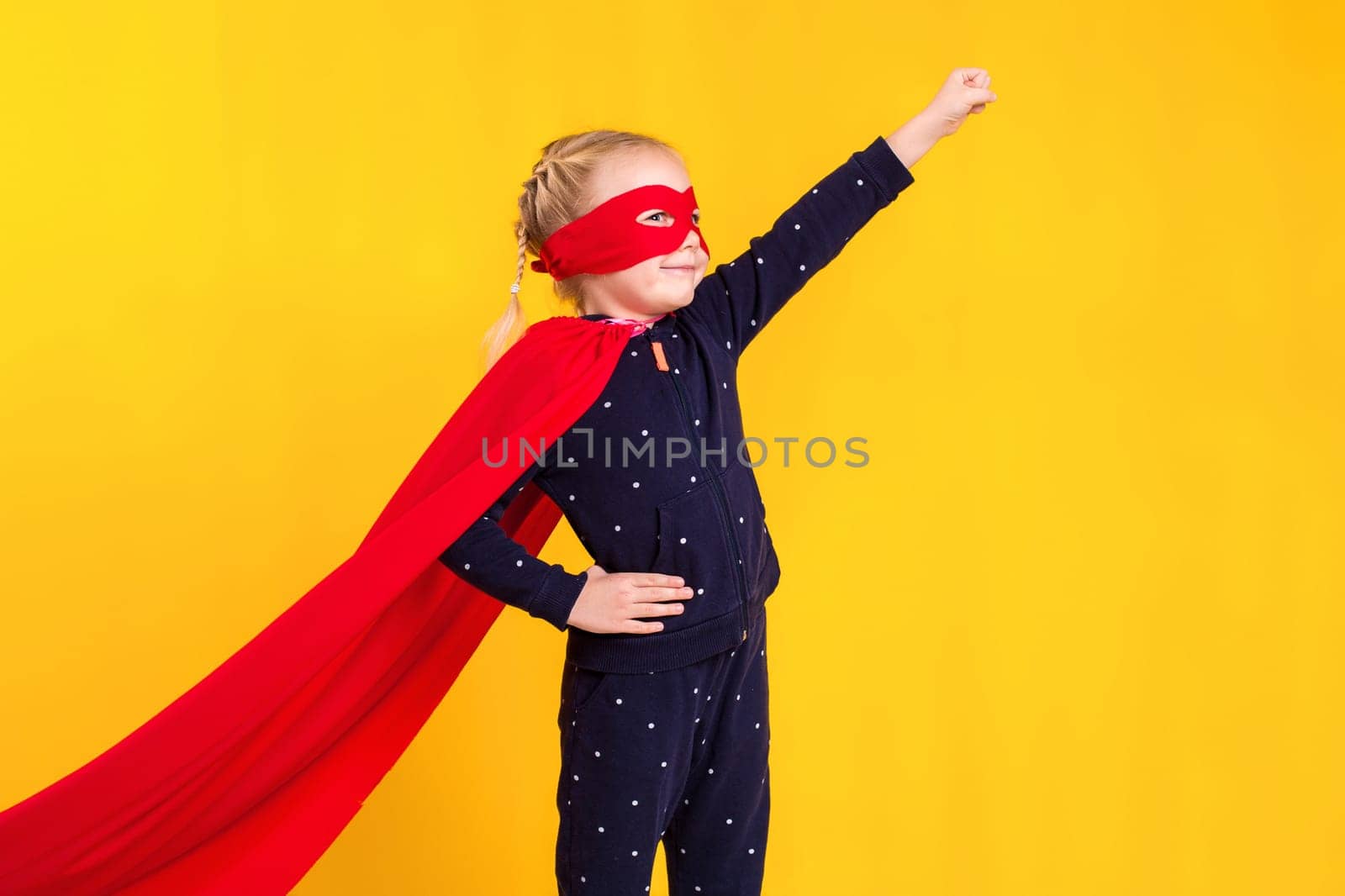 Superhero little girl in a red raincoat and a mask on a yellow background. Studio photography