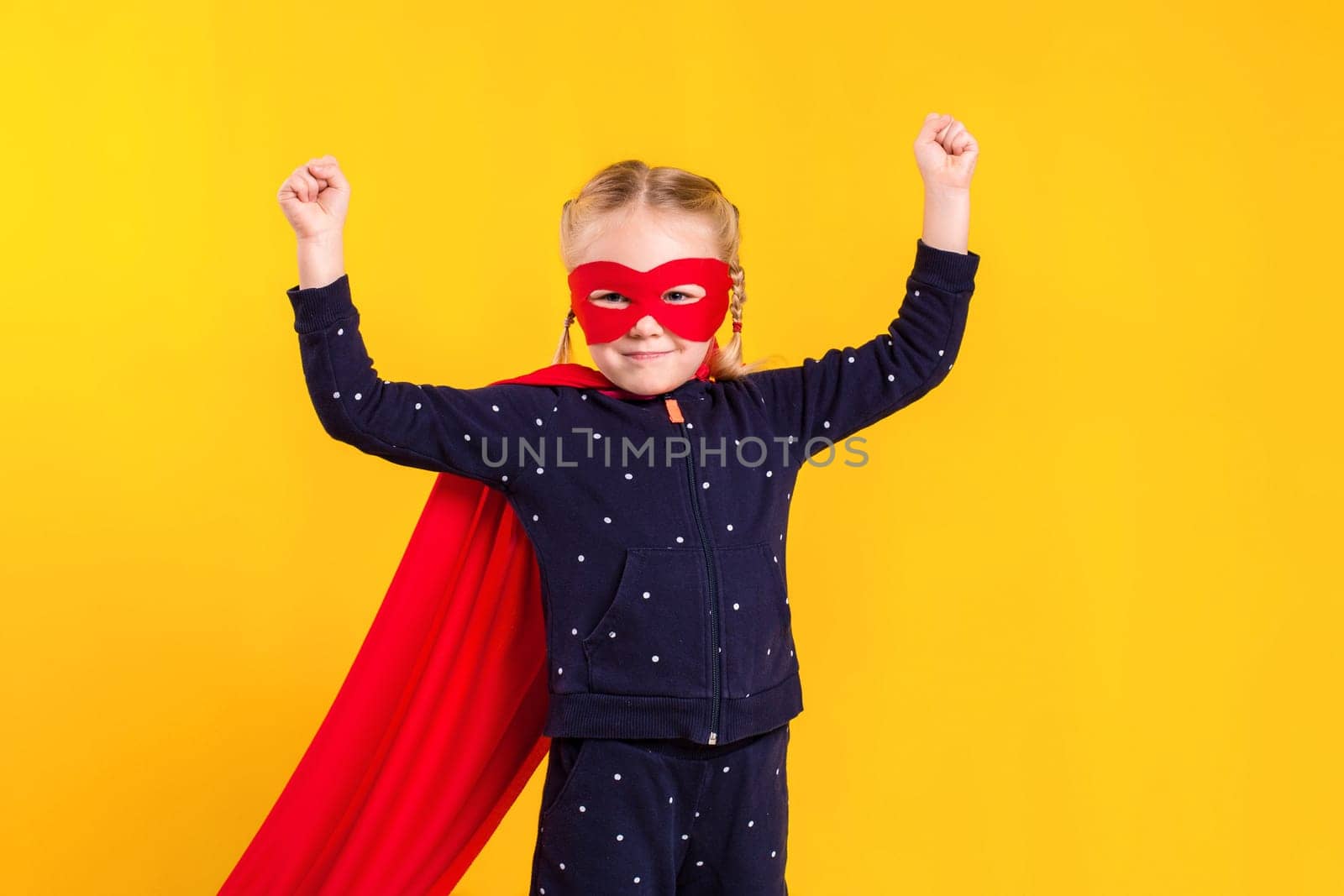 Superhero little girl in a red raincoat and a mask on a yellow background. Studio photography