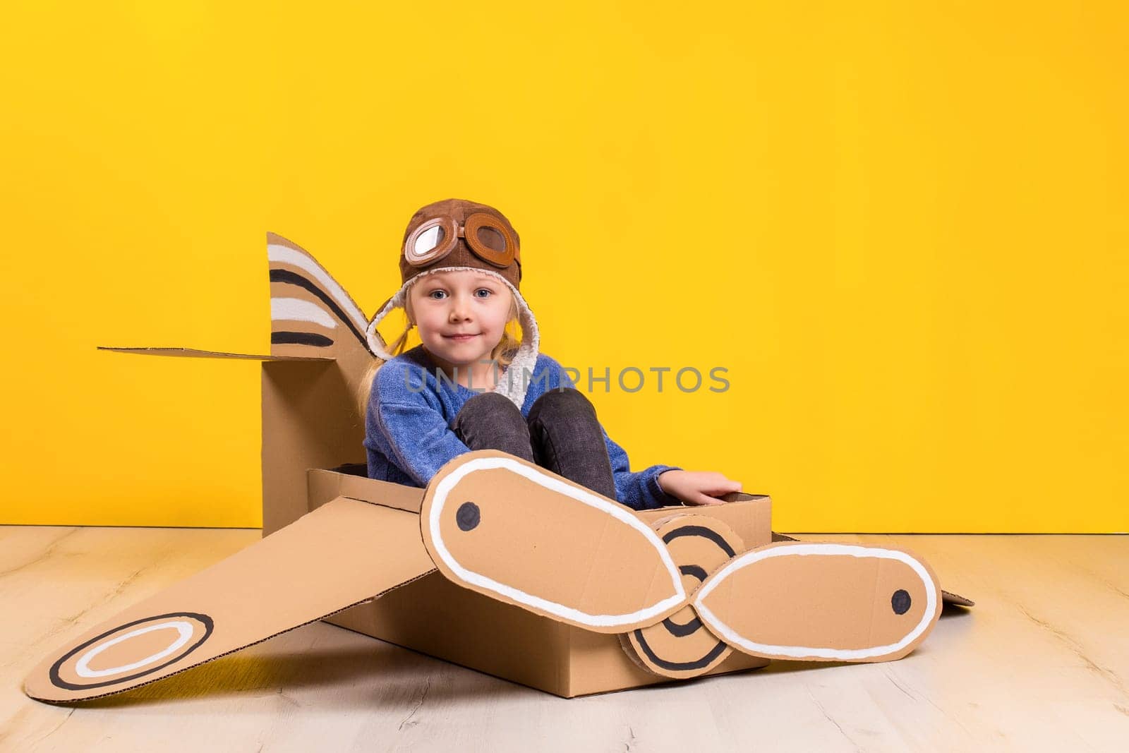 Little dreamer girl playing with a cardboard airplane. Childhood. Fantasy, imagination. Studio photography on a yellow background. Imagination or exploration concept