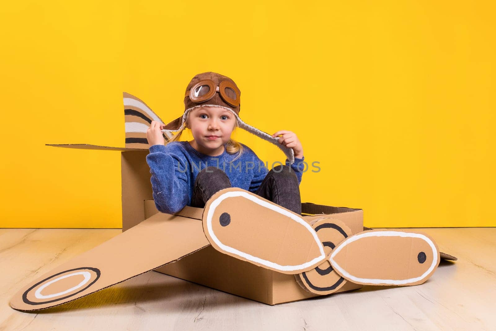Little dreamer girl playing with a cardboard airplane. Childhood. Fantasy, imagination. Studio photography on a yellow background. Imagination or exploration concept