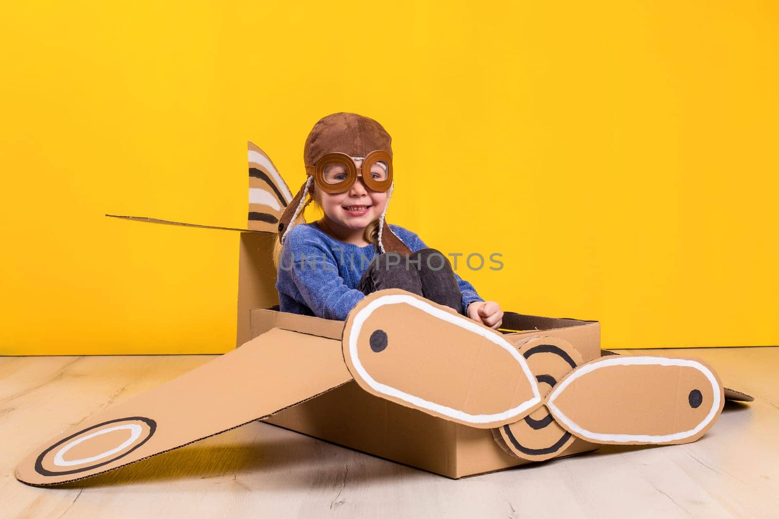 Little dreamer girl playing with a cardboard airplane. Childhood. Fantasy, imagination. Studio photography on a yellow background. Imagination or exploration concept