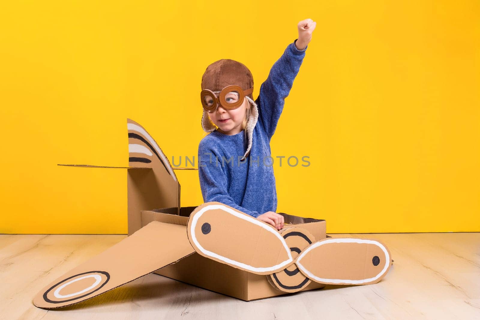 Little dreamer girl playing with a cardboard airplane. Childhood. Fantasy, imagination. Studio photography on a yellow background. Imagination or exploration concept