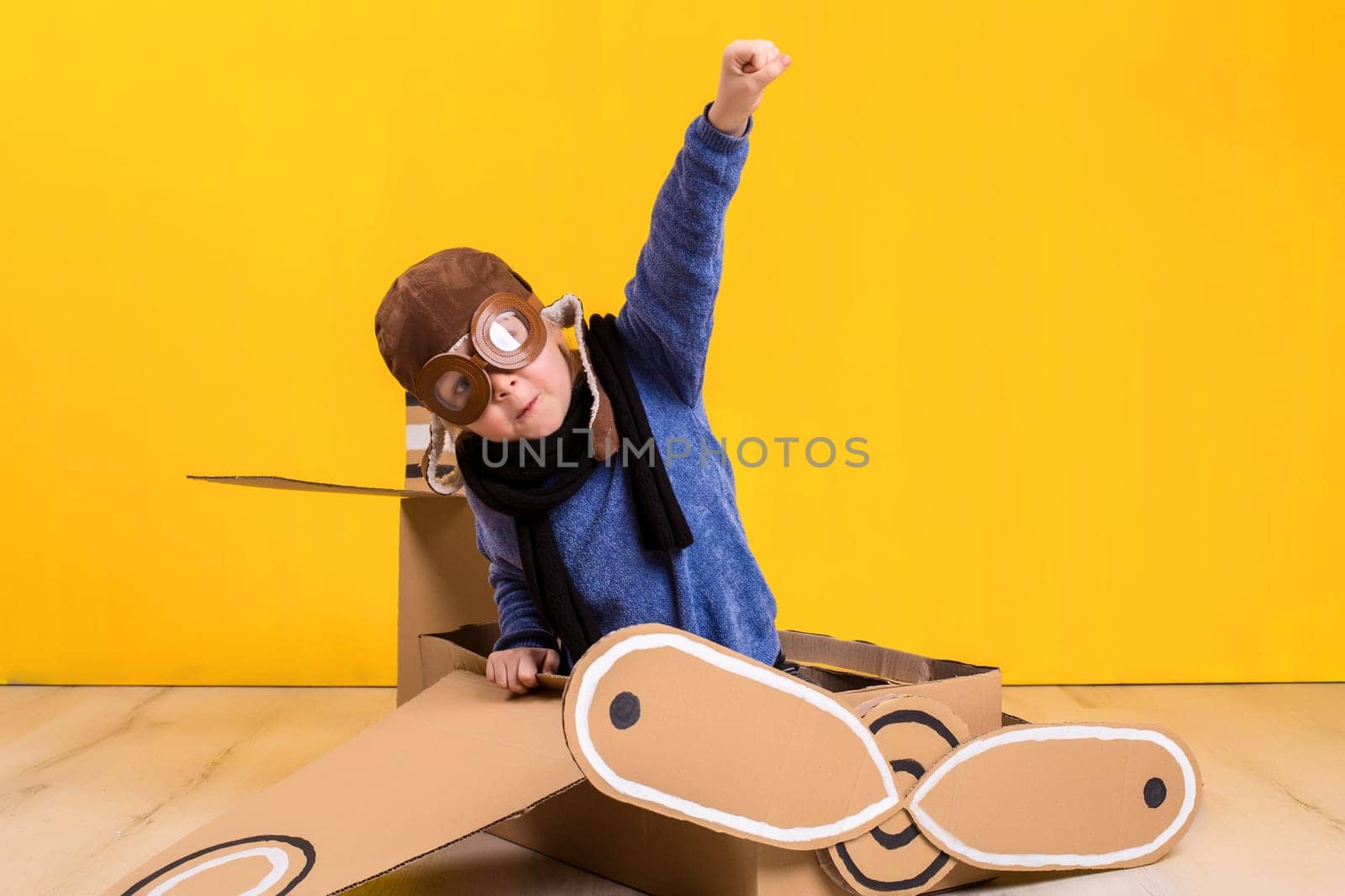 Little dreamer girl playing with a cardboard airplane. Childhood. Fantasy, imagination. Studio photography on a yellow background. Imagination or exploration concept