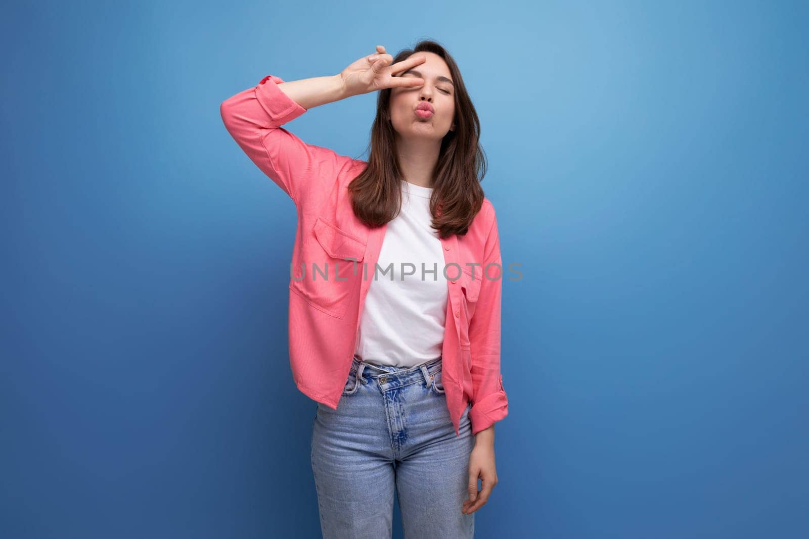 young woman in a pink shirt and jeans with a smile on a studio isolated background by TRMK
