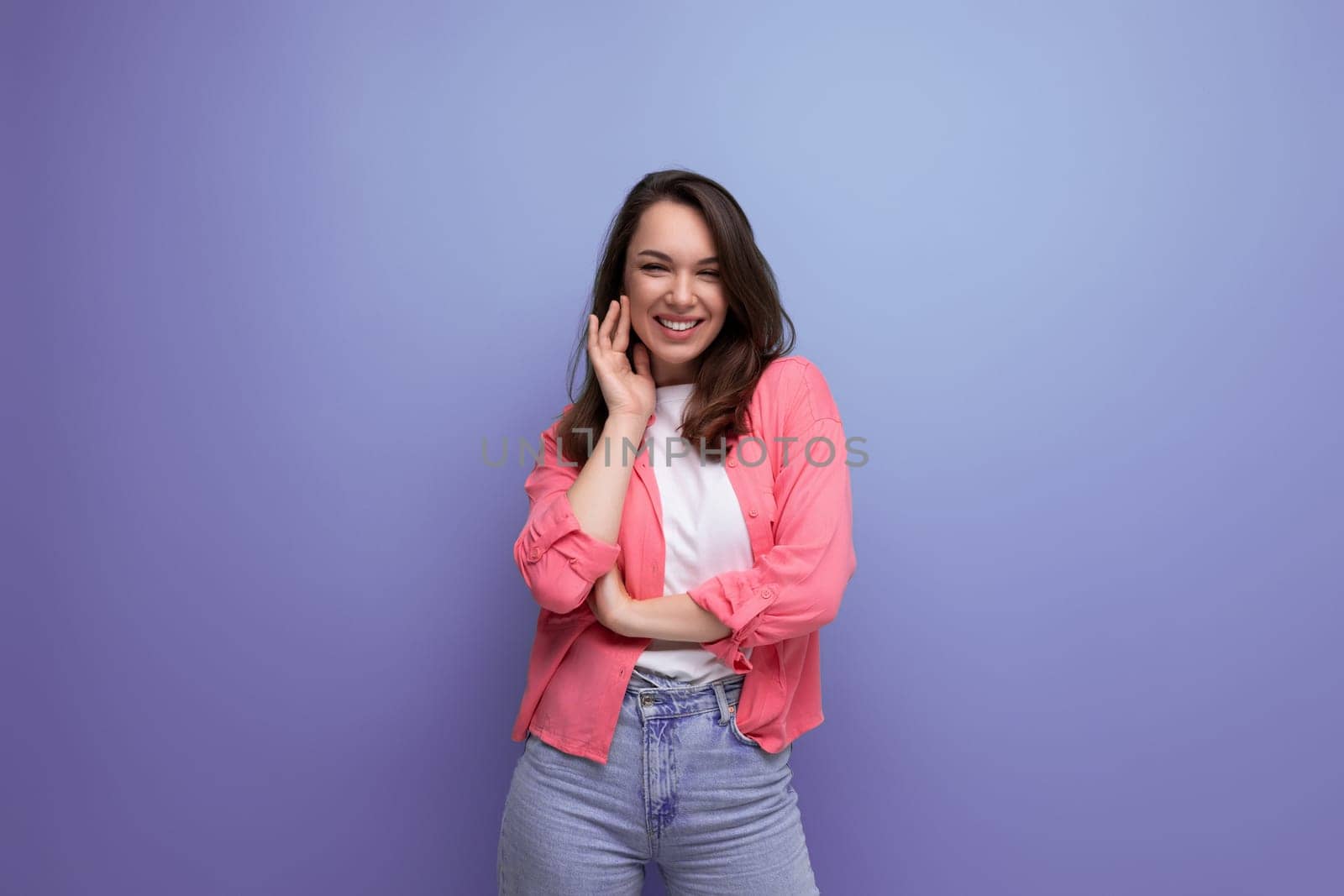 portrait of a brunette woman in a shirt and jeans posing with a smile on a studio background.