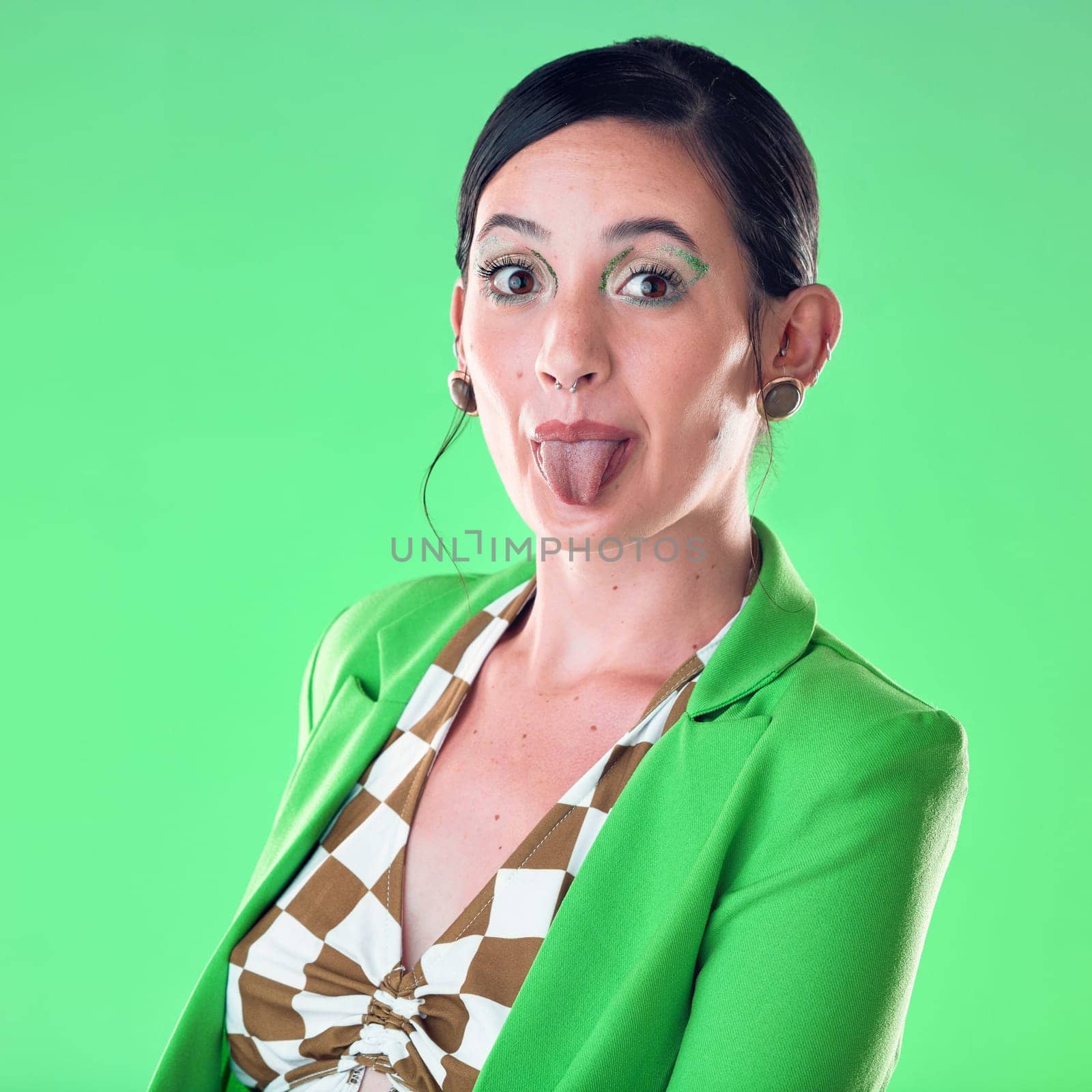 Portrait, fashion and woman with tongue out in studio isolated on a green background. Comic face, funny and gen z female model with makeup, cosmetics or beauty aesthetics, trendy or stylish suit