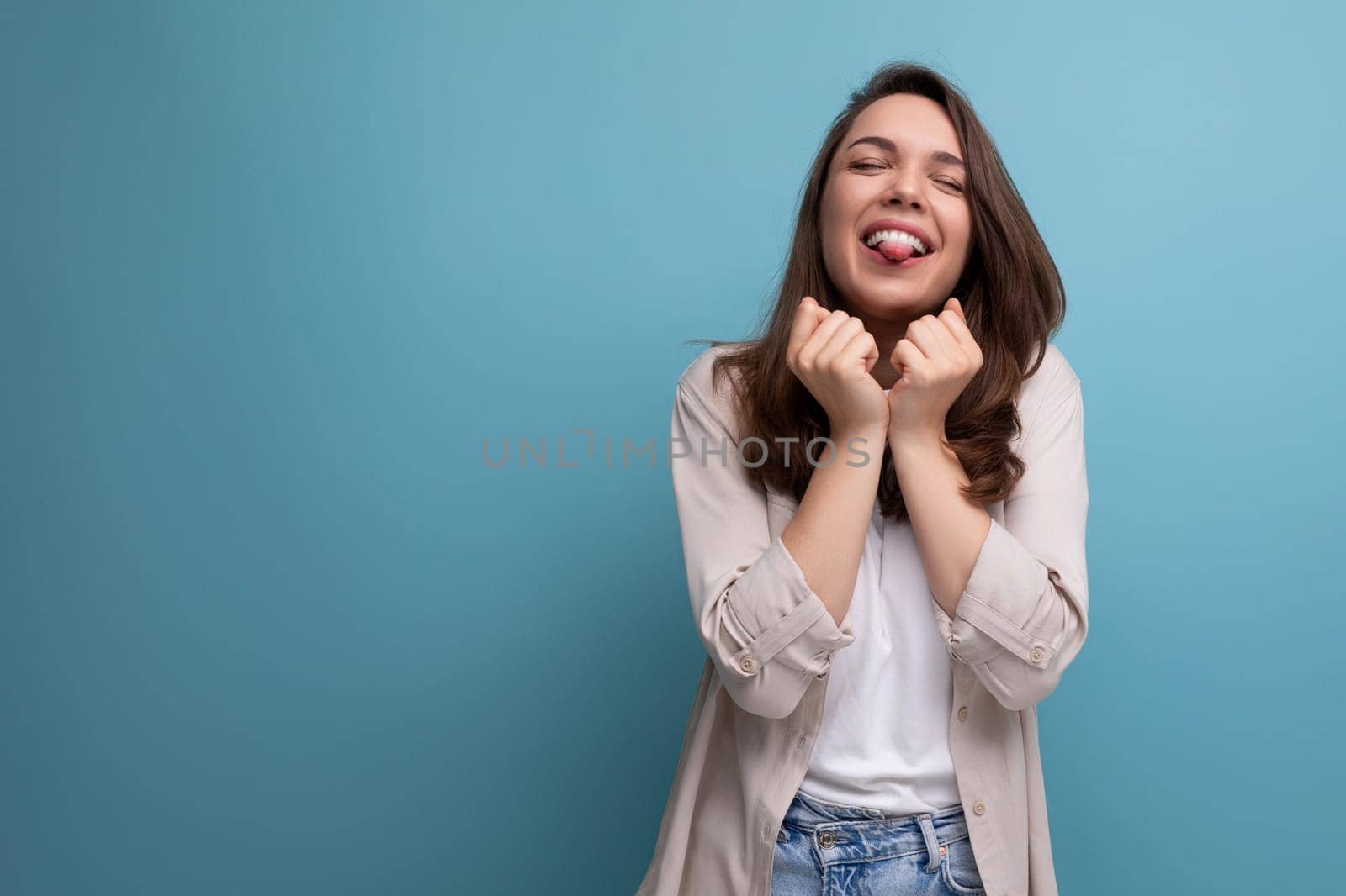 joyful happy young dark-haired lady in informal clothes celebrating victory on blue background.