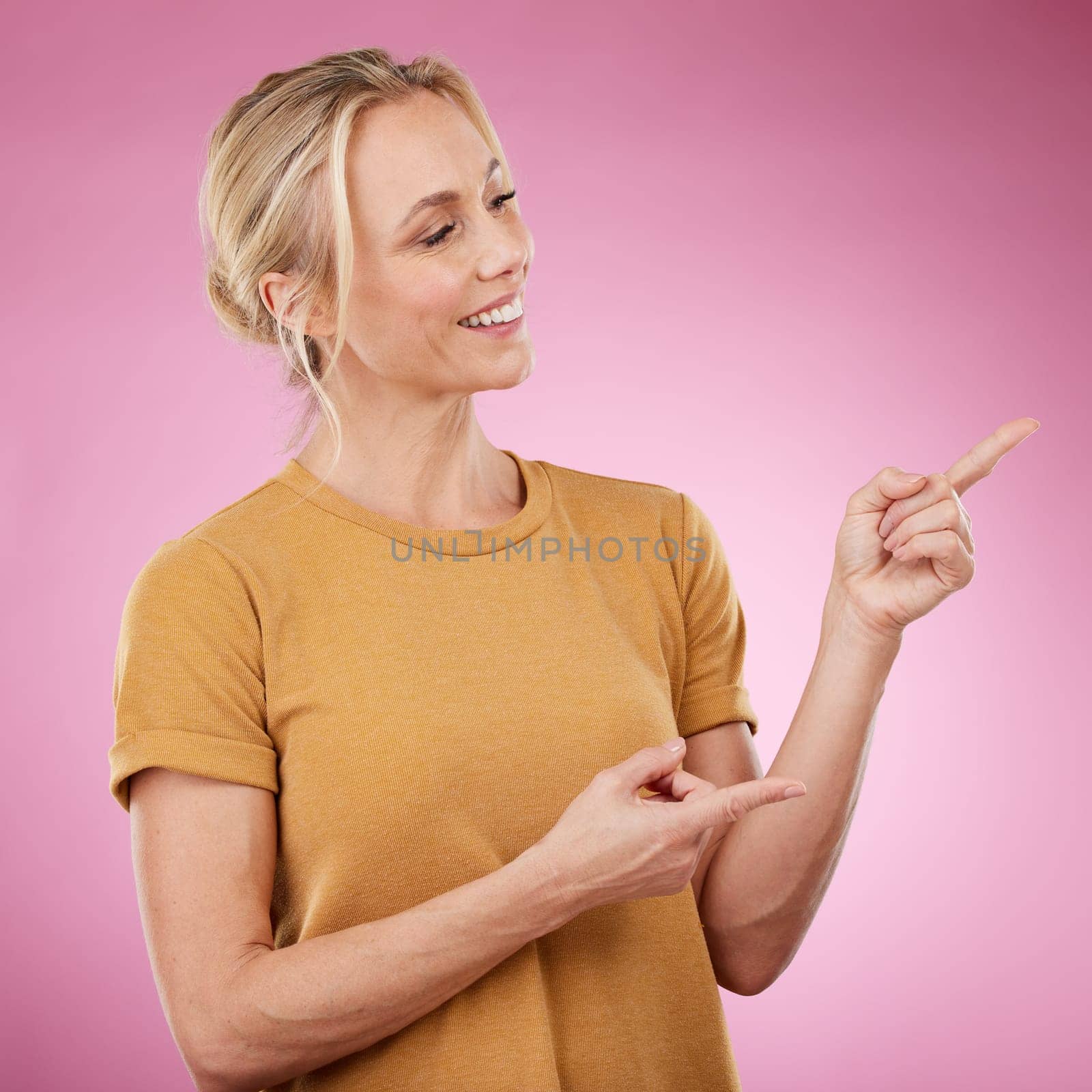 Happy, pointing and female model in studio to mockup for advertisement or product placement. Happiness, excited and woman from Canada showing with her finger mock up for marketing by pink background