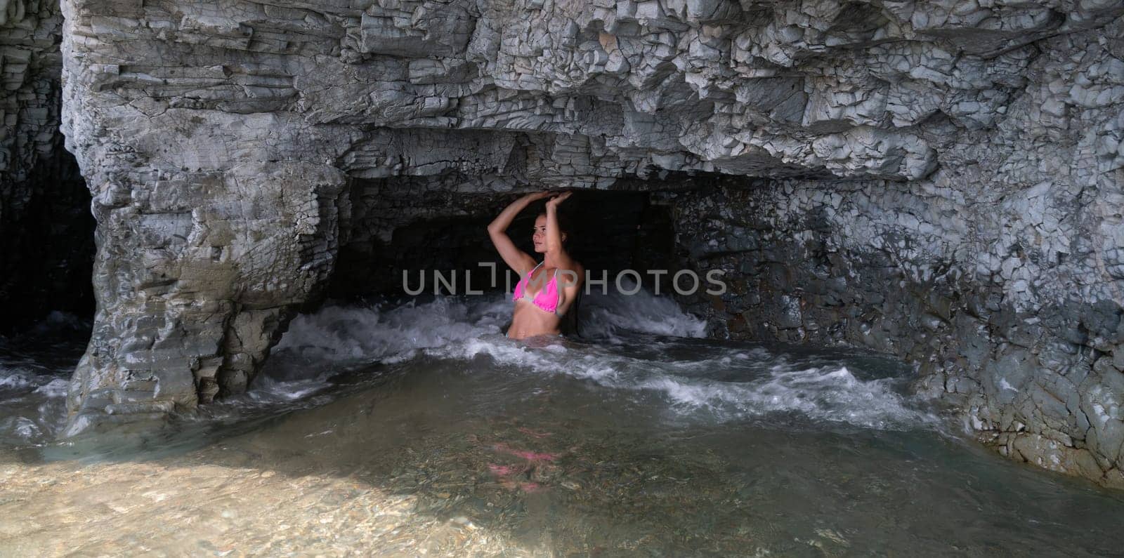 Woman travel sea. Young Happy woman in a long red dress posing on a beach near the sea on background of volcanic rocks, like in Iceland, sharing travel adventure journey