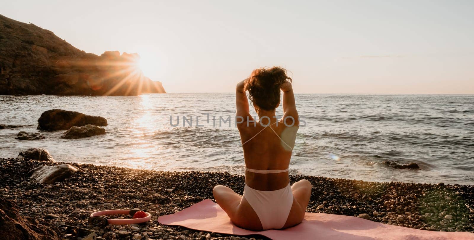 Woman sea yoga. Happy woman in white swimsuit and boho style braclets practicing outdoors on yoga mat by sea on sunset. Women yoga fitness routine. Healthy lifestyle, harmony and meditation by panophotograph