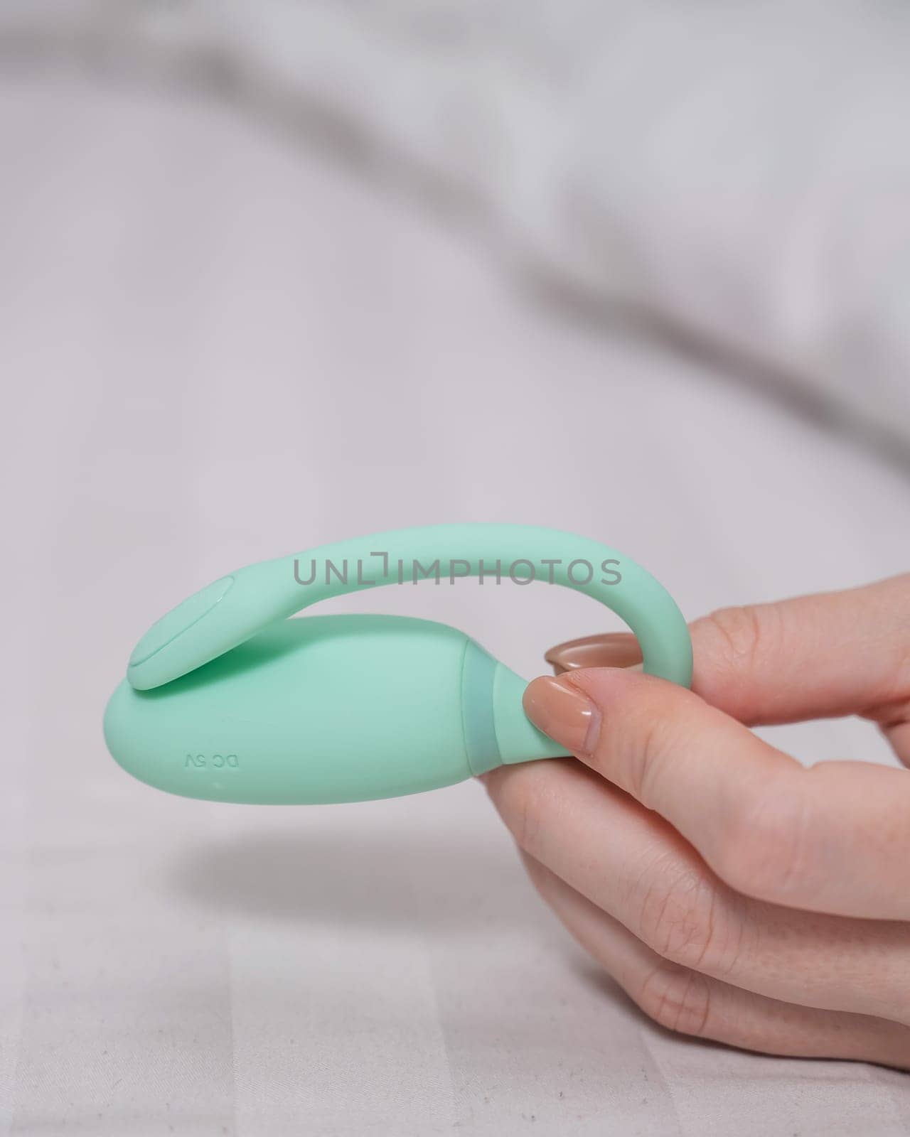 Woman holding mint vibrator while lying on white sheet