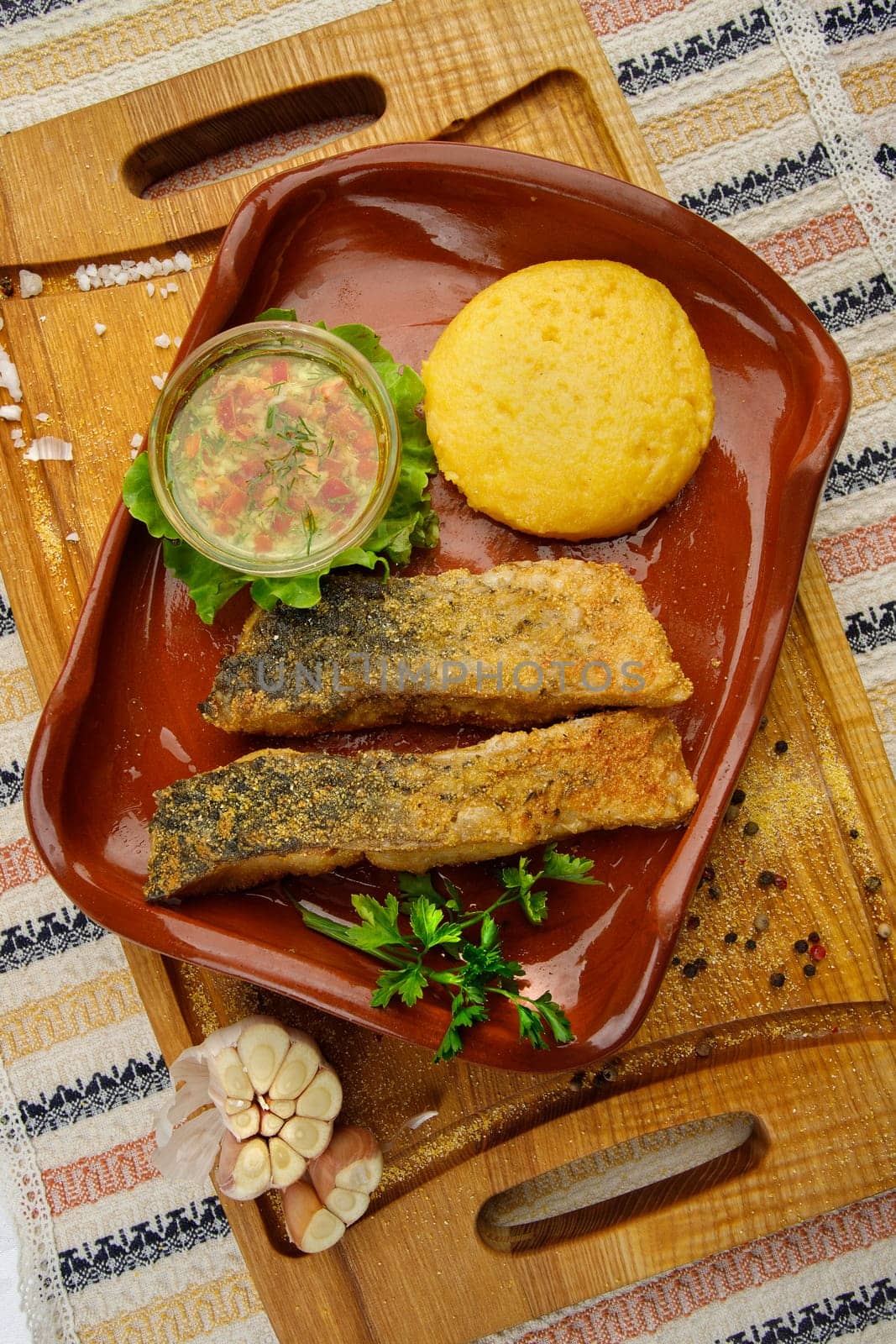 Whole fried fish in a red plate served with mamaliga and garlic souce