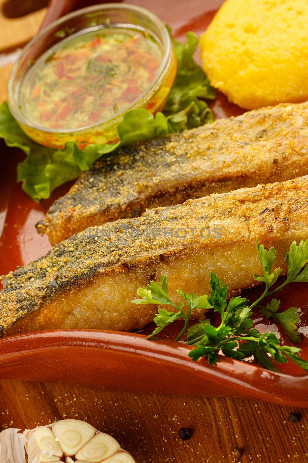 Whole fried fish in a red plate served with mamaliga and garlic souce