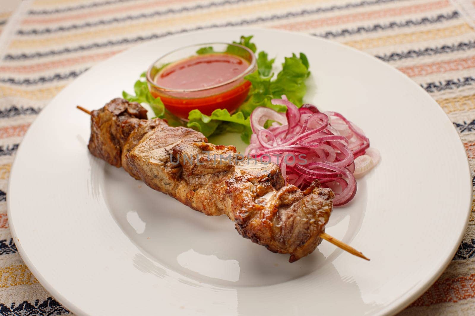 Grilled pork kebab with red onion and chilly souce on a white plate