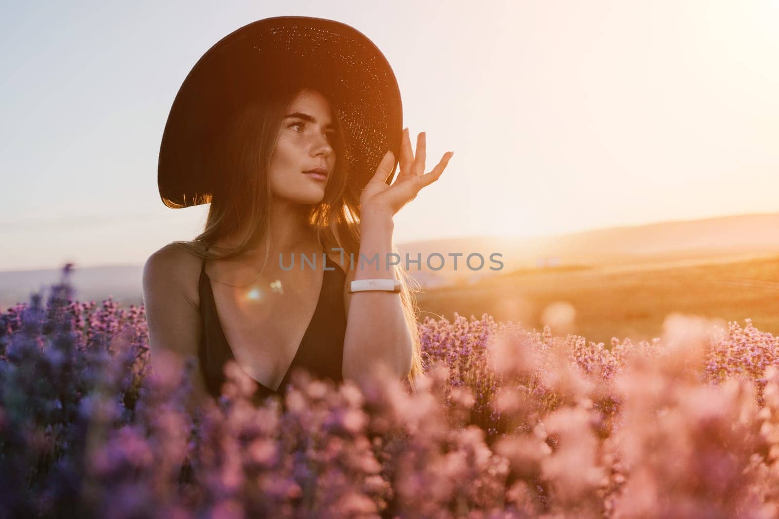 Woman lavender field. Happy carefree woman in black dress and hat with large brim walking in a lavender field during sunset. Perfect for inspirational and warm concepts in travel and wanderlust. by panophotograph