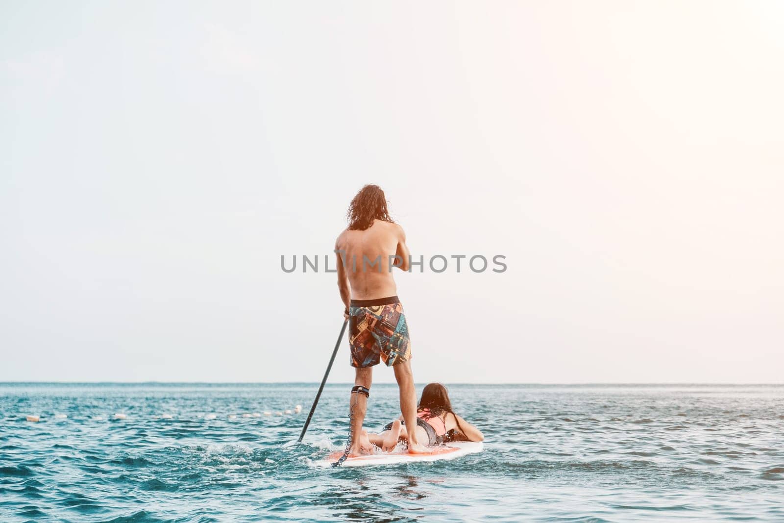 Silhouette of woman standing, surfing on SUP board, confident paddling through water surface. Idyllic sunset or sunrise. Sports active lifestyle at sea or river.