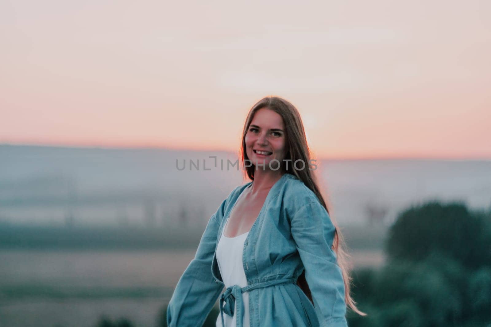Romantic beautiful bride in white dress posing with sea and mountains in background. Stylish bride standing back on beautiful landscape of sea and mountains on sunset