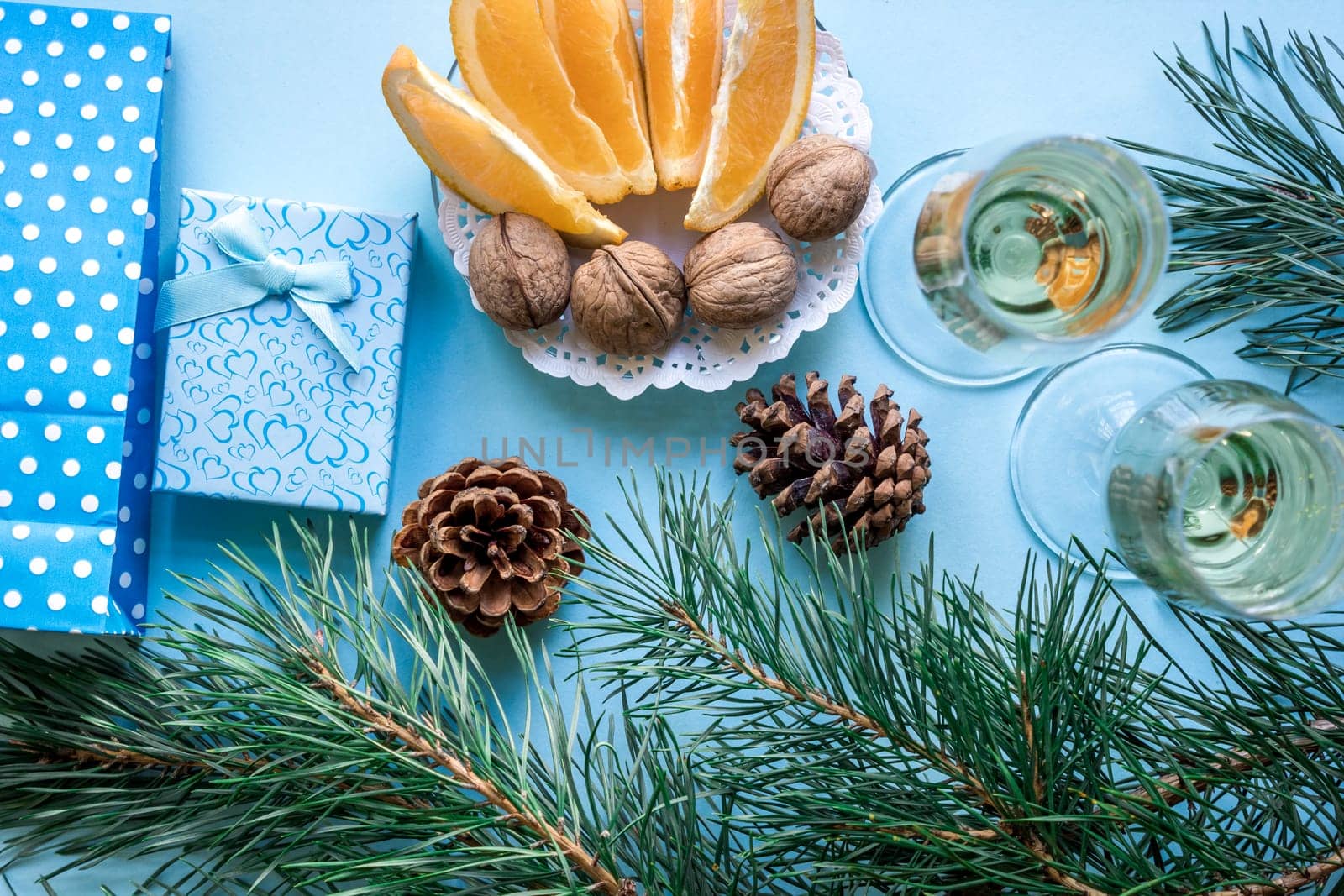 New Year's holiday with spruce branches, Christmas presents and with a pair of wine glasses of champagne on blue background. Flat lay, top view, copy space