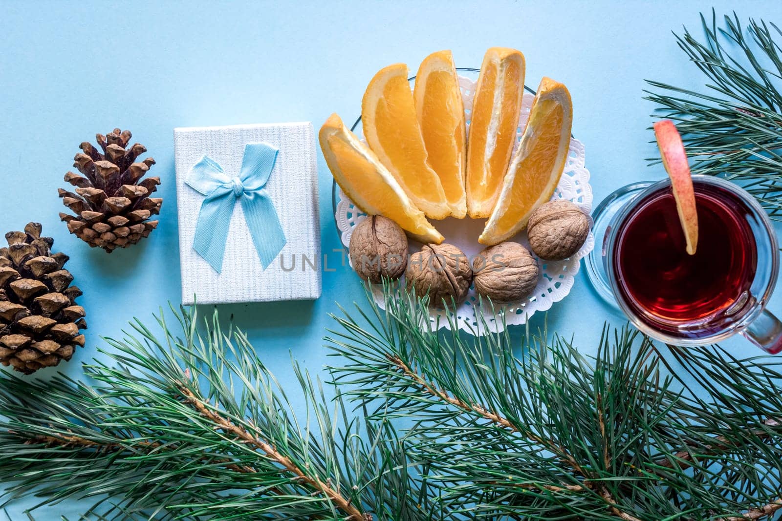 Hot mulled wine with orange, anise, cardamon and cinnamon on blue background. Christmas tree branches, gifts and cones. Flat lay, copy space, top view. Holidays.