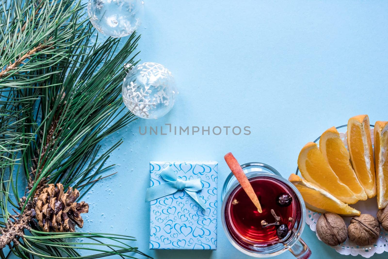 Hot mulled wine with orange, anise, cardamon and cinnamon on blue background. Christmas tree branches, gifts and cones. Flat lay, copy space, top view. Holidays.