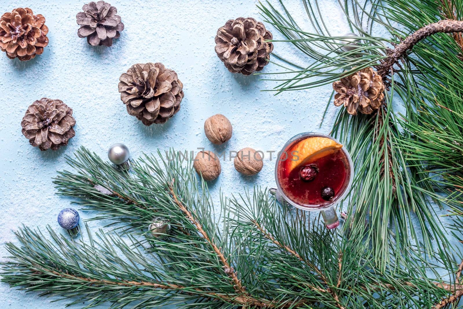 Hot mulled wine with orange, anise, cardamon and cinnamon on blue background. Christmas tree branches, gifts and cones. Flat lay, copy space, top view. Holidays.