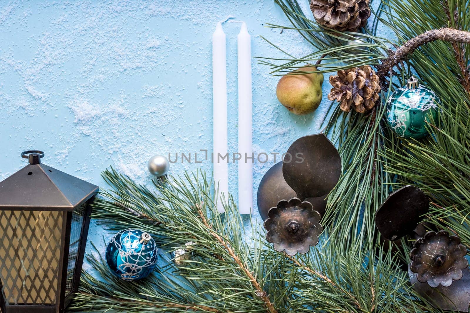 Christmas decoration. Branch christmas tree and cones spruce, antique candlesticks, candles, glass balls on snow on blue background. Top view, flat lay
