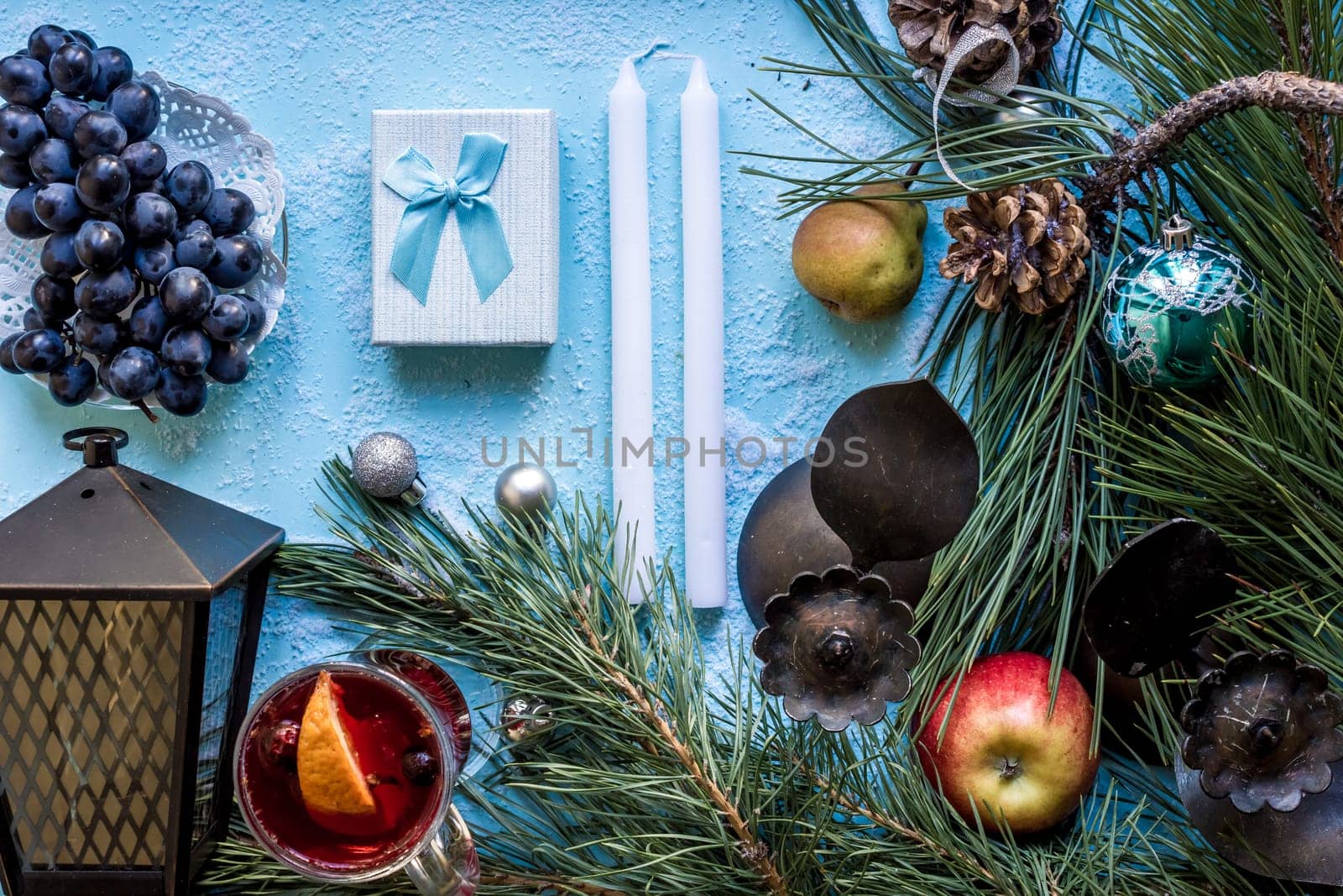 Hot mulled wine with orange, anise, cardamon and cinnamon on blue background. Christmas tree branches, gifts and cones. Flat lay, copy space, top view. Holidays.