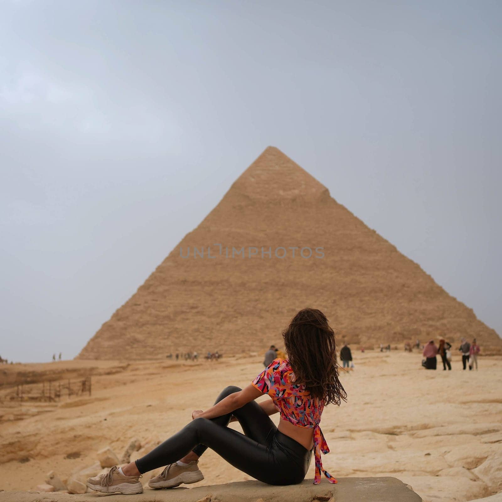 Beautiful brunette girl sitting in front of and looking at the Pyramid of Giza. High quality photo