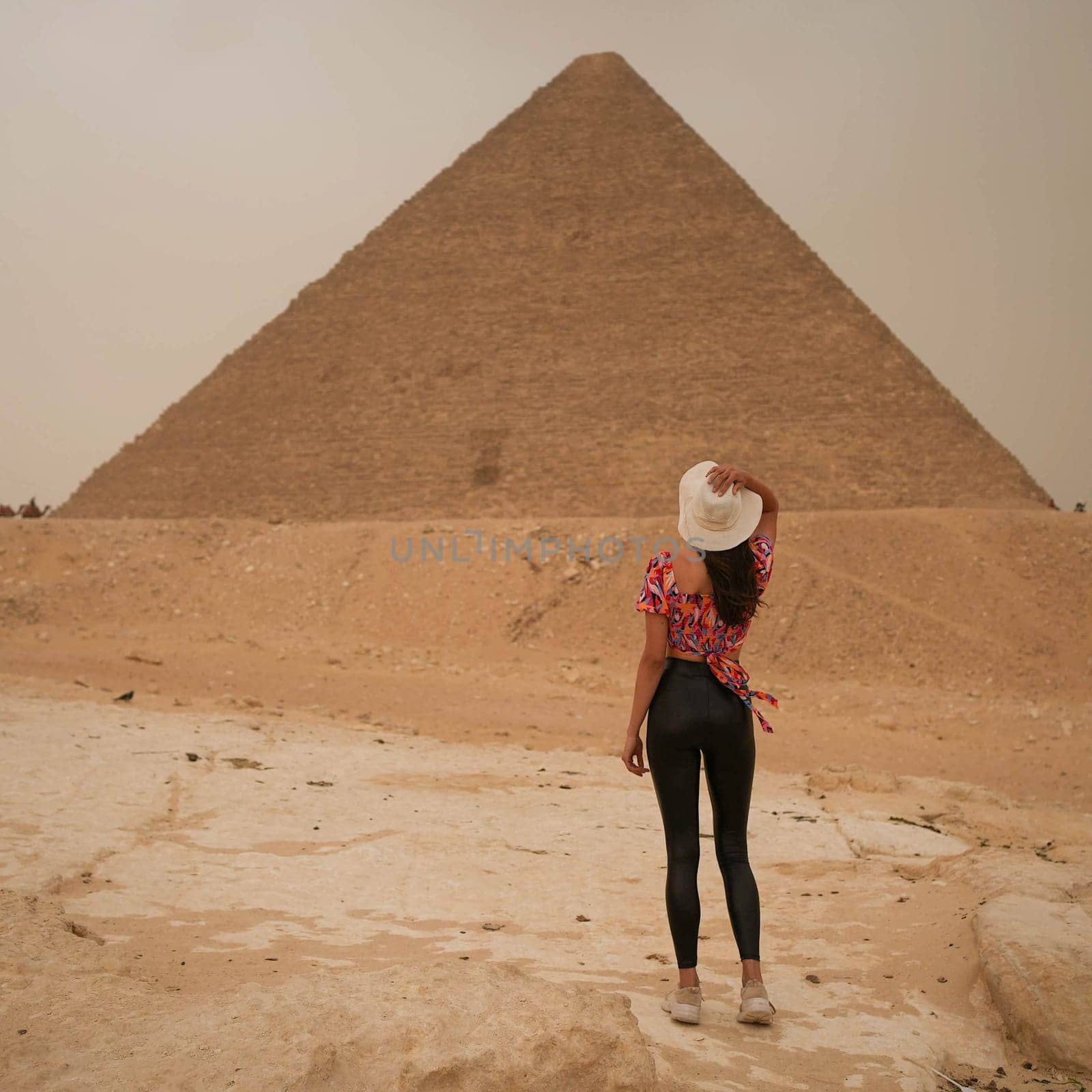 Young Beautiful Tall Girl in front of the Egyptian pyramid of Giza in white straw hat with storm approaching. High quality photo