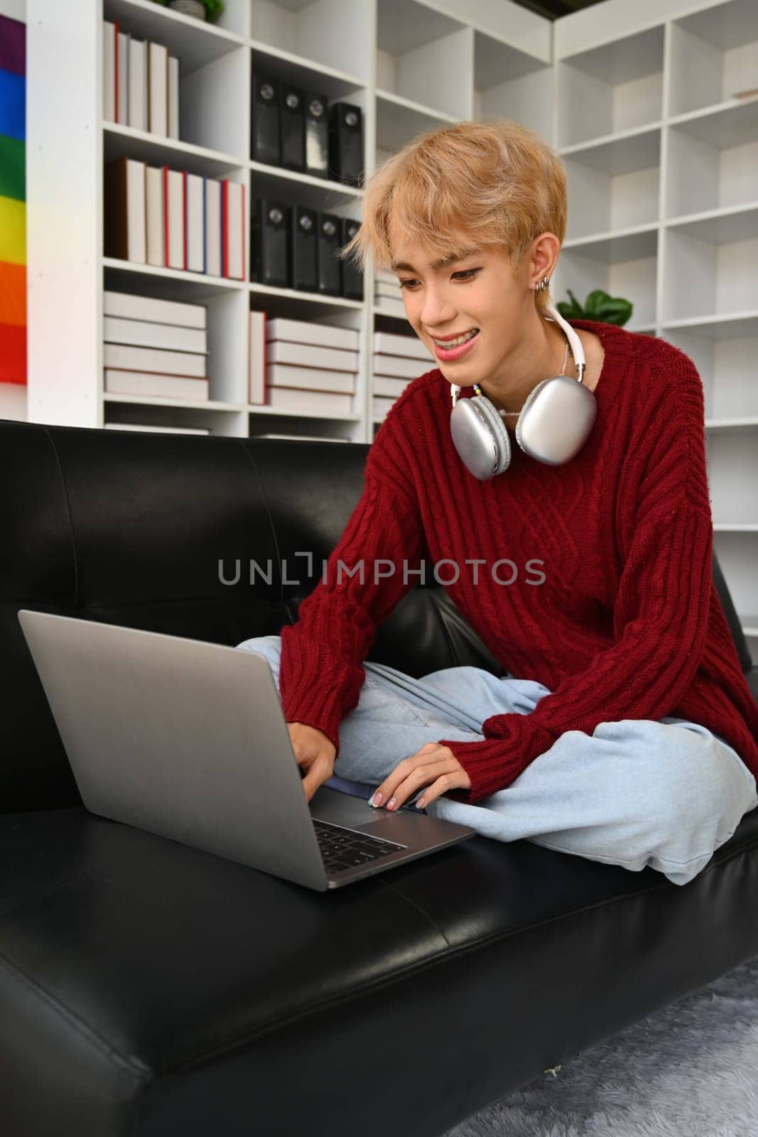 Cheerful asian gay man sitting on couch and using laptop, typing on keyboard, chatting on social media or shopping online.