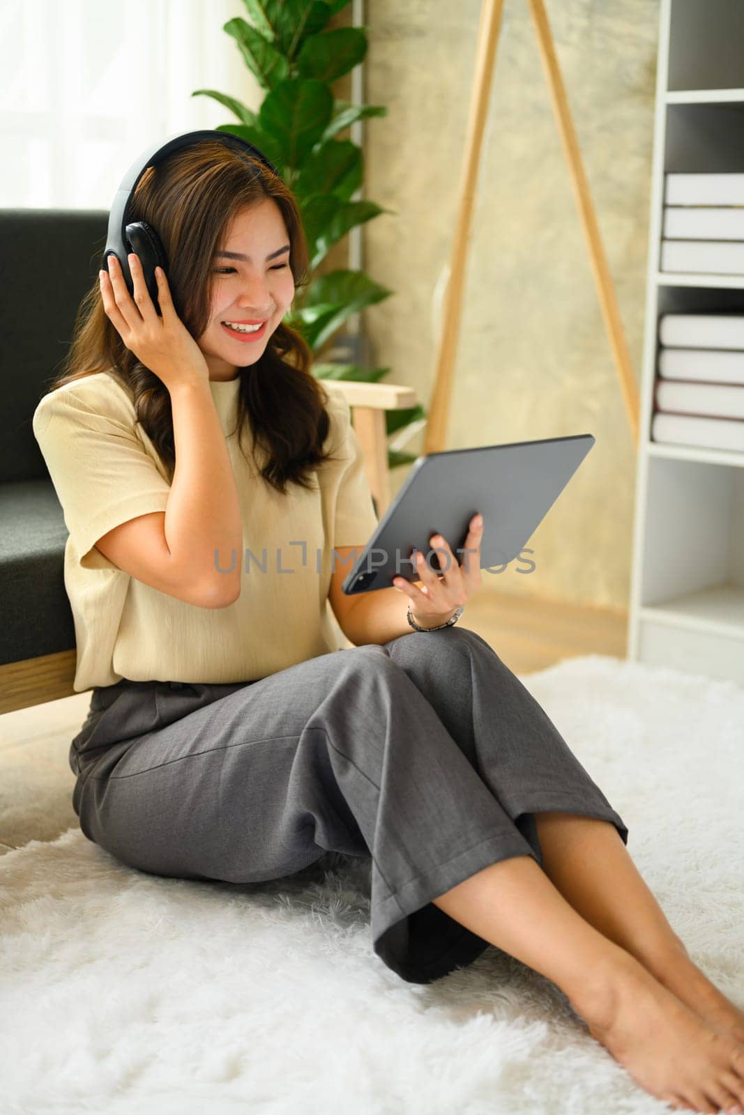 Happy young woman wearing headphones, using digital tablet in living room, listening to music, watching video, podcast.