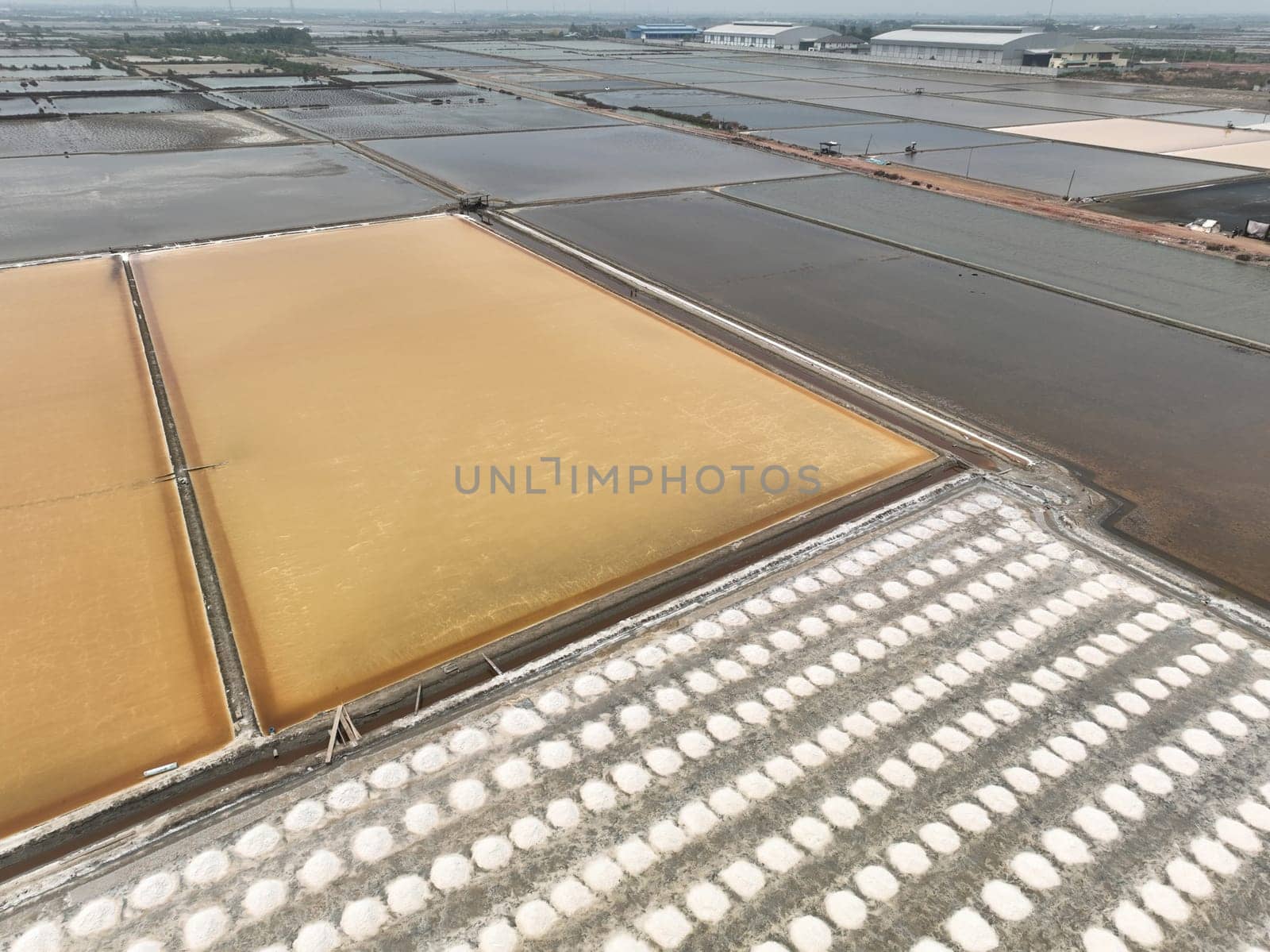 Aerial top view sea salt farm. Pile of brine salt. Raw material of salt industrial. Sodium Chloride mineral. Evaporation and crystallization of sea water. White salt harvesting. Agriculture industry.