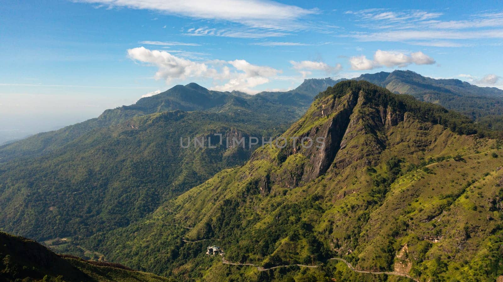 Aerial view of Mountains covered with forest against a background of blue sky and clouds. Mountainous terrain in Sri Lanka.