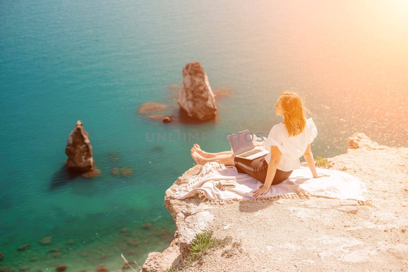 Freelance woman working on a laptop by the sea, typing away on the keyboard while enjoying the beautiful view, highlighting the idea of remote work. by Matiunina