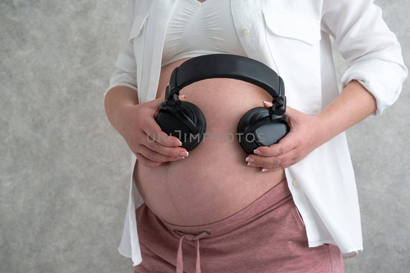 Pregnant woman putting headphones on her belly. Concept of listening music before birth by Mariakray