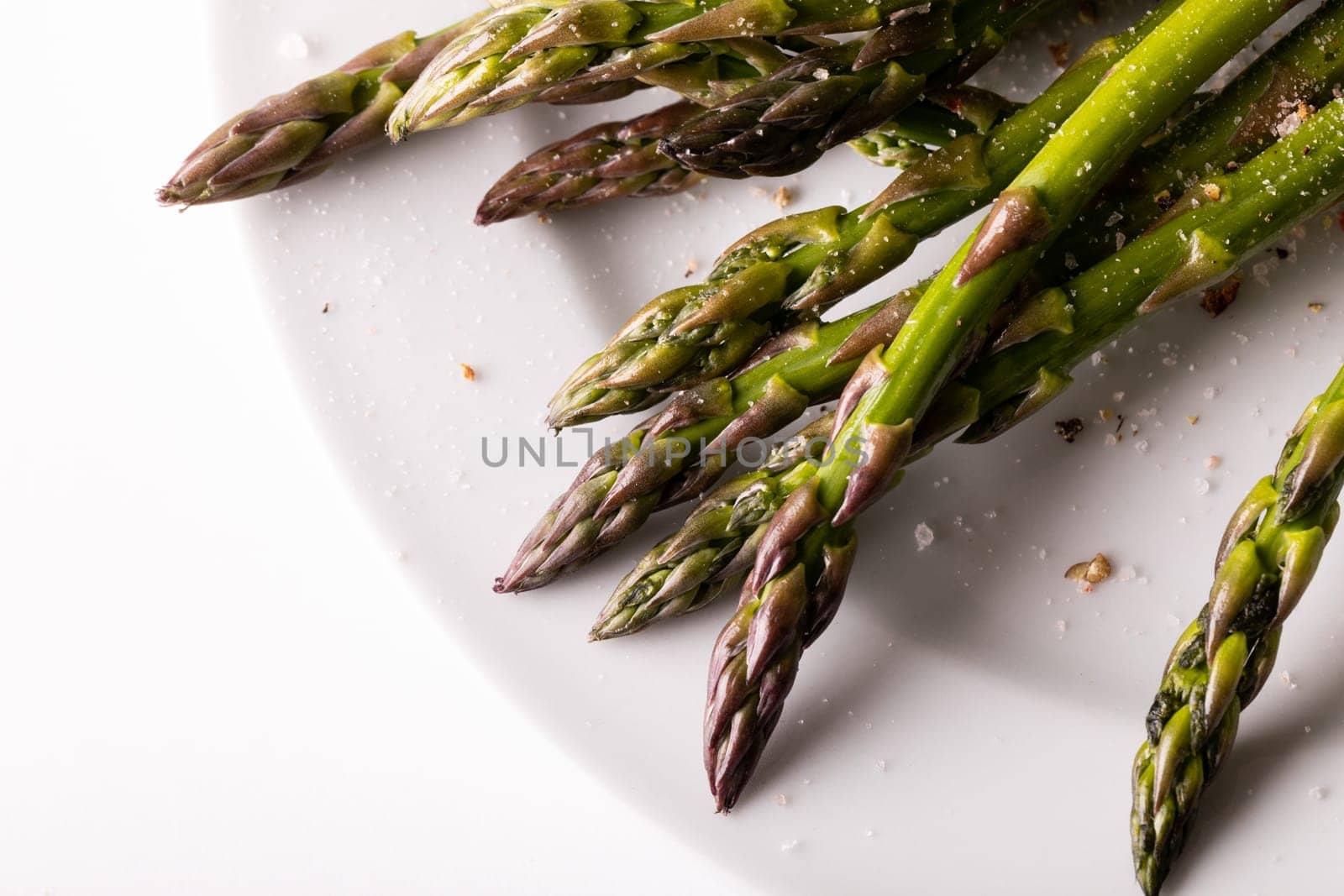 High angle close-up view of asparagus and seasoning in plate on white background. unaltered, food, healthy eating and organic concept.