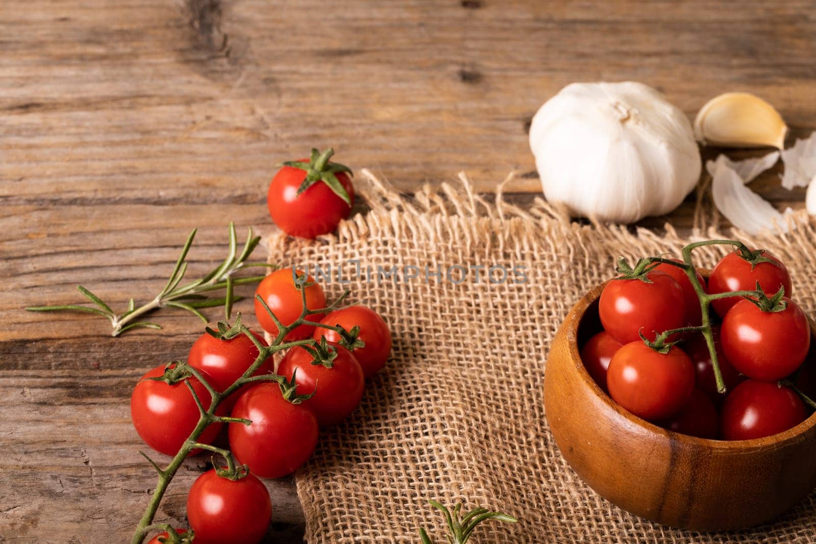 High angle view of fresh cherry tomatoes with garlic bulb and burlap on wooden table. unaltered, organic food and healthy eating concept.