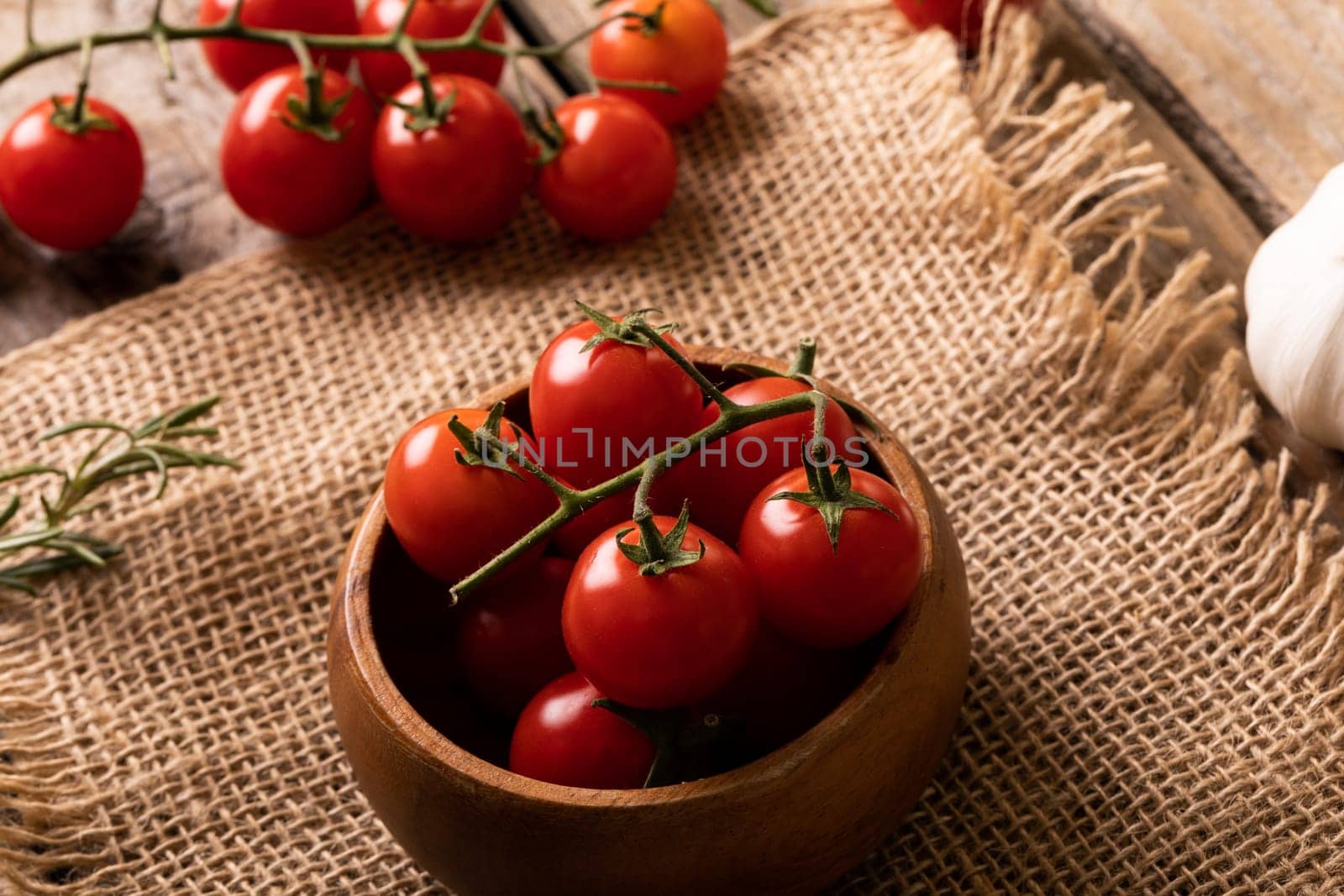 High angle view of fresh red cherry tomatoes in wooden bowl over burlap. unaltered, organic food and healthy eating concept.