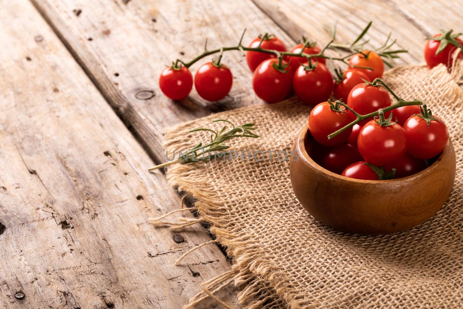 High angle view of fresh red cherry tomatoes and wooden bowl with burlap on table. unaltered, organic food and healthy eating concept.