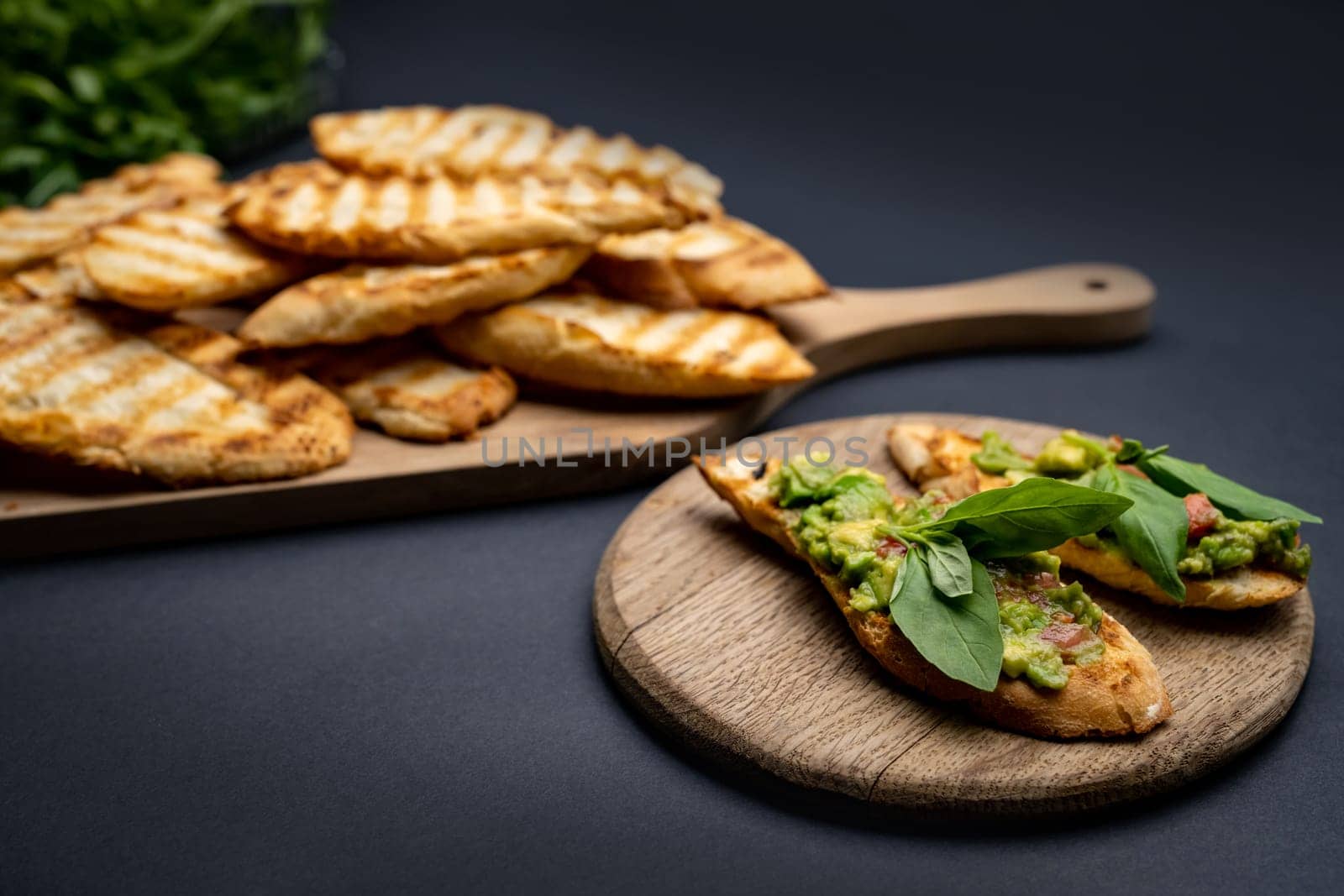 Bruschettas with toast, guacamole, basil and cherry tomatoes on wooden board. Mexican snack slice bread with avocado, herbs and vegetables
