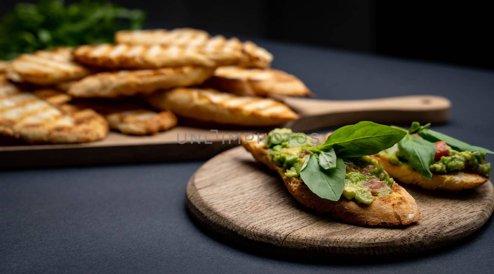 Bruschettas with toast, guacamole, basil and cherry tomatoes on wooden board. Mexican snack slice bread with avocado, herbs and vegetables