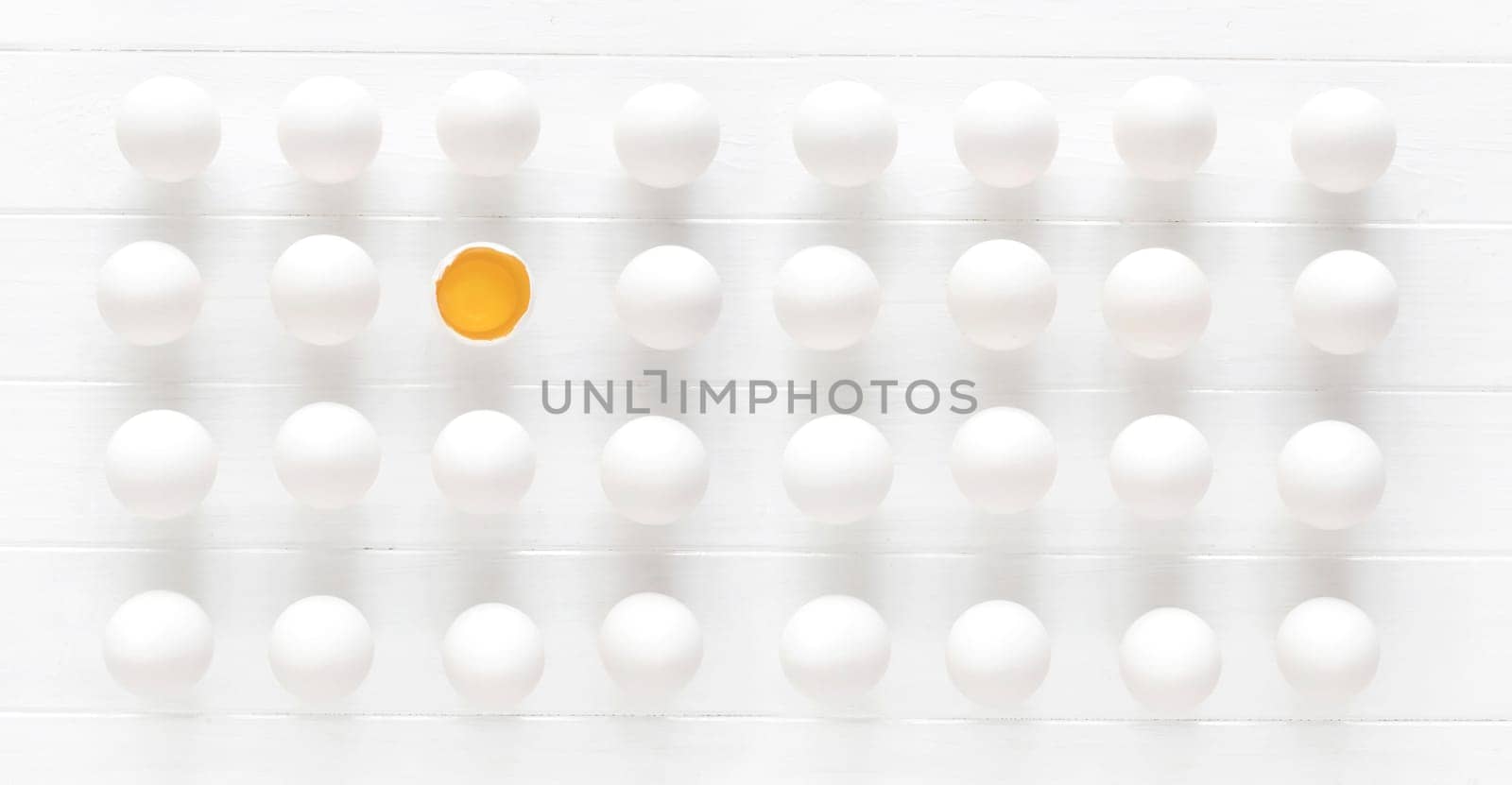 White raw eggs rows with one yolk on a white wooden table