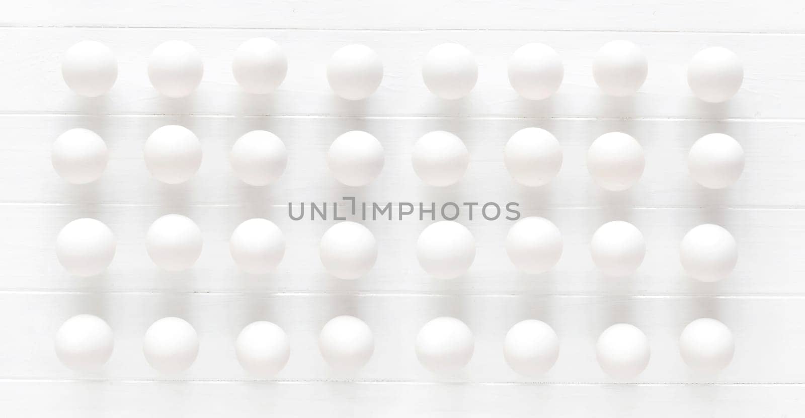 White raw eggs rows on a white wooden table view from above