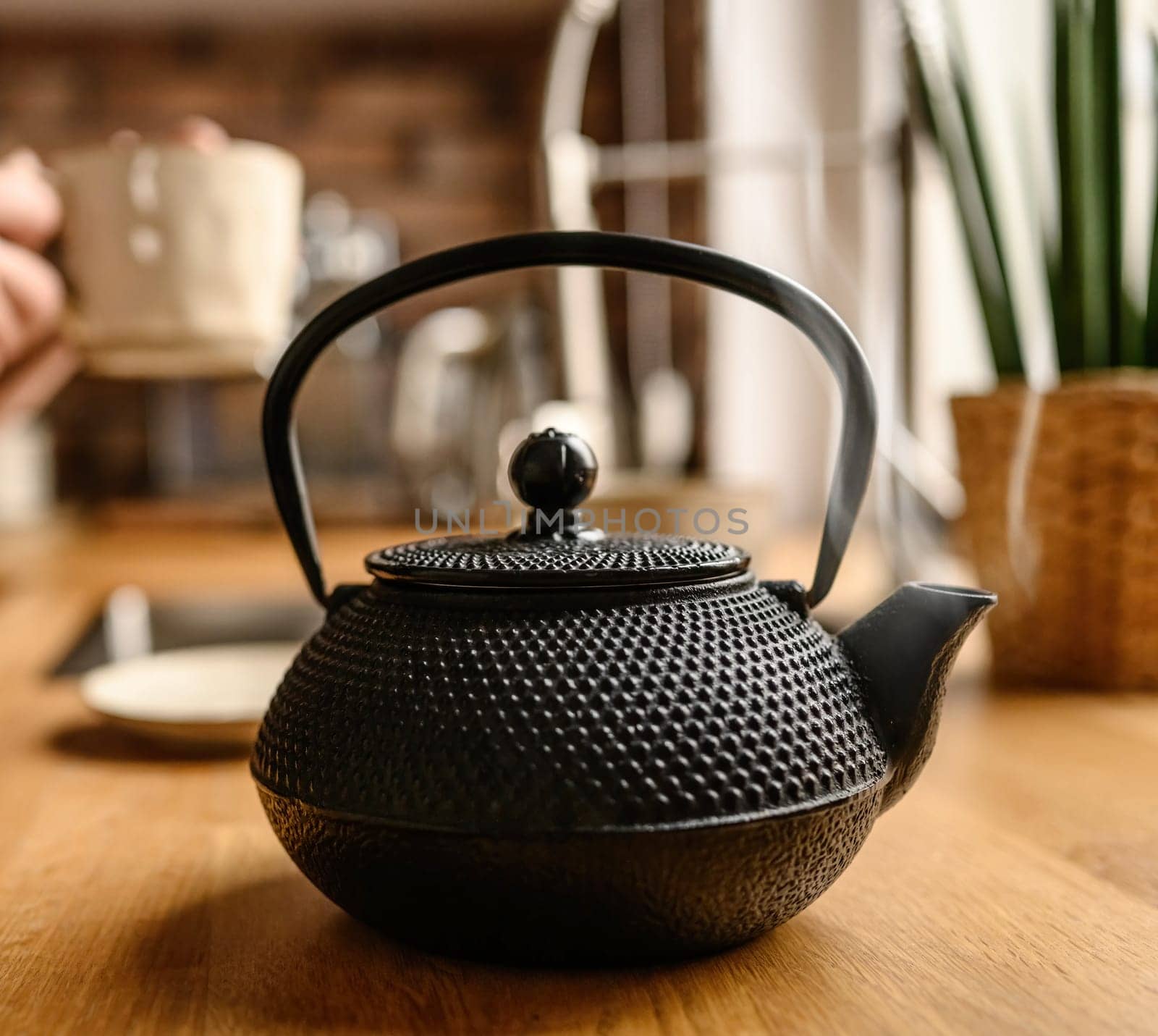 Black metal teapot with hot tea at the kitchen. Steam comes from the tea spout. Tea drinking traditions. Girl making a tea.