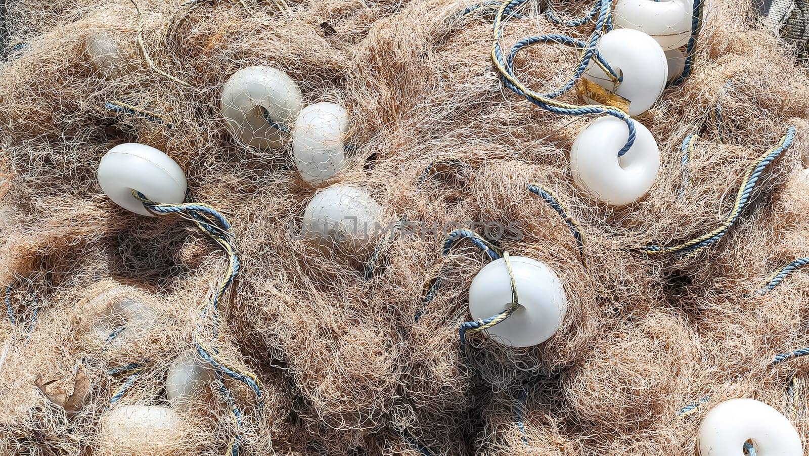 Heap of fishing nets with white floats and ropes lies on ground, top view