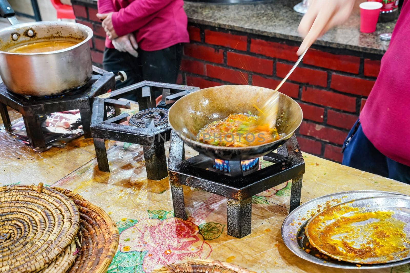 Food being prepared on simple gas stoves in typical Pakistani restaurant, herbs and spices dropped into steel pan with hot dish, closeup detail.