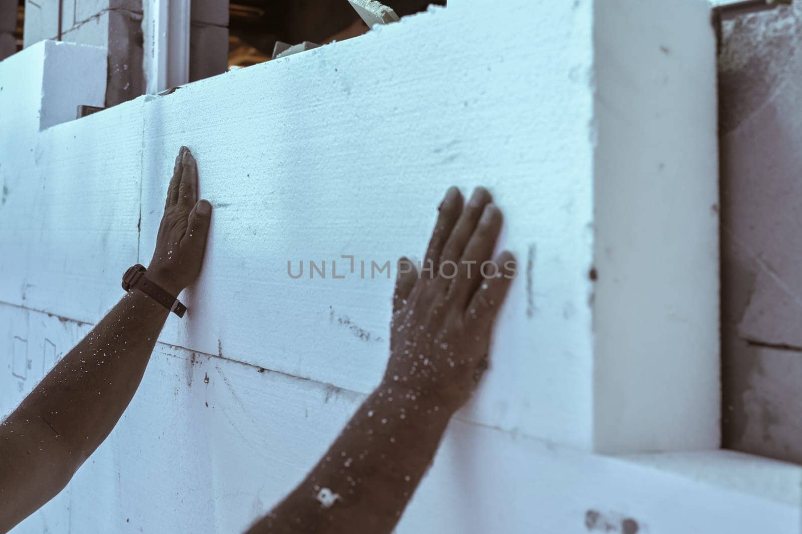Worker installing polystyrene heat insulation on bare house walls, detail to hand touching white foam boards.