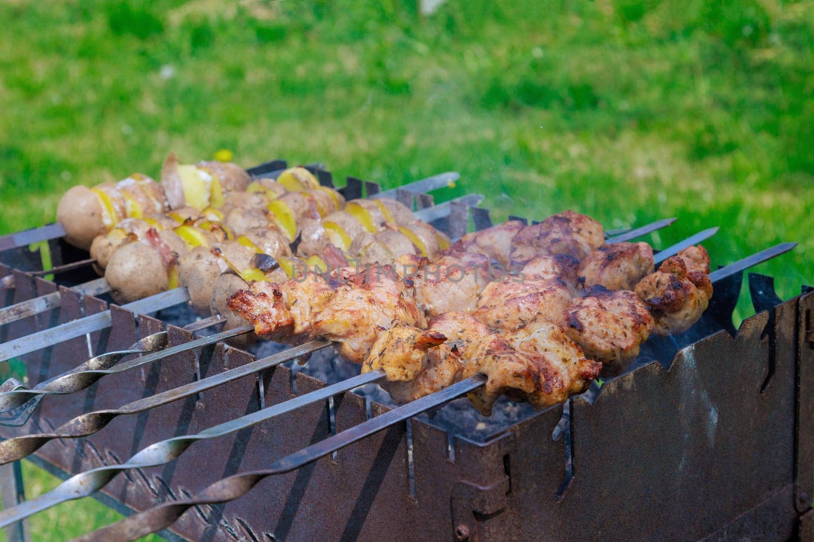 Kebab skewers and potatoes with bacon are grilled on portable metal BBQ brazier
